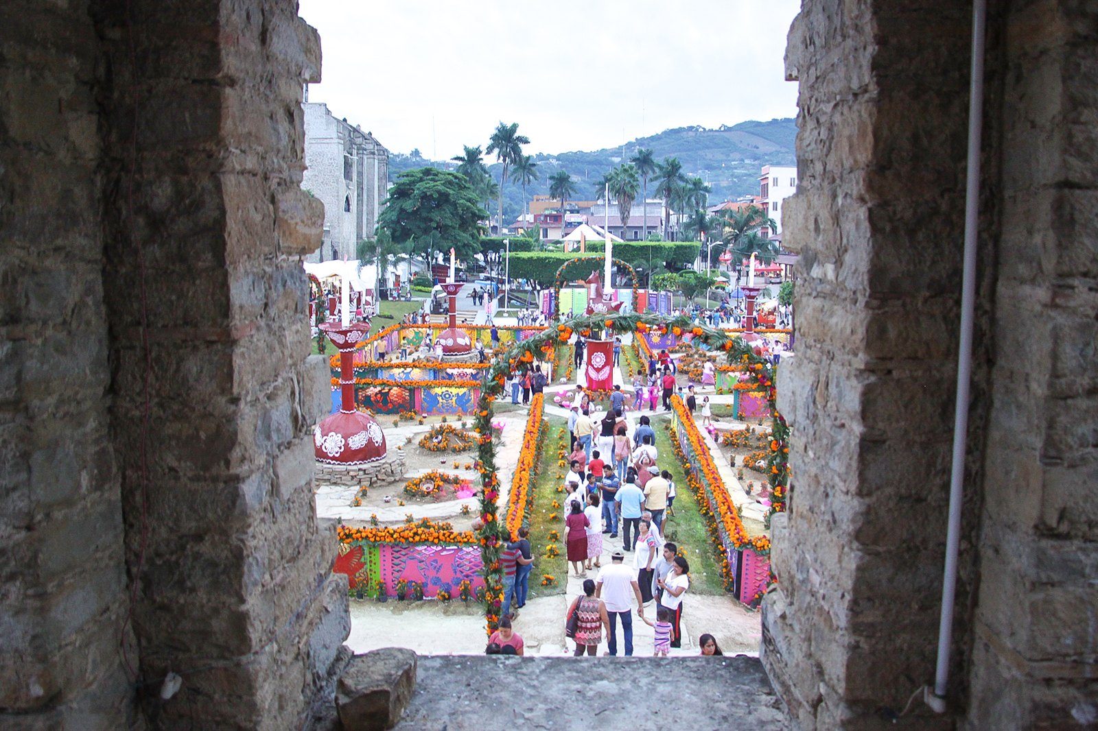 Plaza de Huejutla de Reyes vista desde un vano de piedra, con arcos y ofrendas de cempasúchil y gente caminando entre ellas